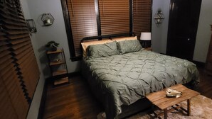 A bedroom with a bed, wooden floor, a ceiling fan, a nightstand, a lamp, and a door. - Classic Build with modern decor (Chattanooga)