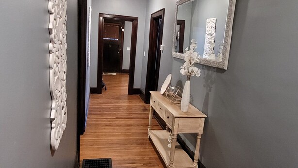 A hallway with a wooden floor, a white decorative wall piece, a mirror, and a small wooden console table with a vase. - Classic Build with modern decor (Chattanooga)