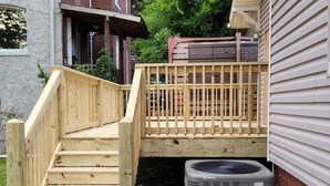 A wooden deck with a staircase leading to a raised platform, an air conditioning unit, and a brick building in the background. - Classic Build with modern decor (Chattanooga)