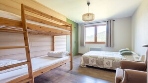Een kamer met stapelbedden, een enkel bed, een stoel, een raam met gordijnen en een hanglamp.