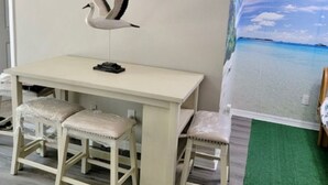 Une pièce avec une table blanche et deux chaises, une décoration représentant une mouette au mur et une fresque murale représentant une scène de plage.