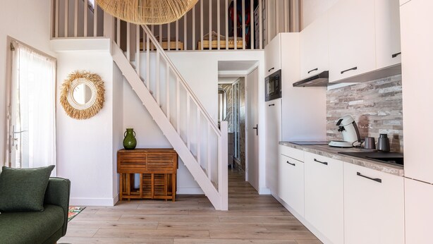 A modern kitchen with white cabinets, a wooden staircase, and a dining area with a green sofa and ottoman.