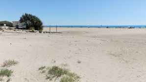 A sandy beach with a small building, sparse vegetation, and the ocean in the background.