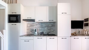 A modern kitchen with white cabinetry, a built-in microwave, and a stone backsplash.