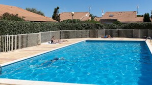 A rectangular swimming pool with a tiled deck, surrounded by a white fence.