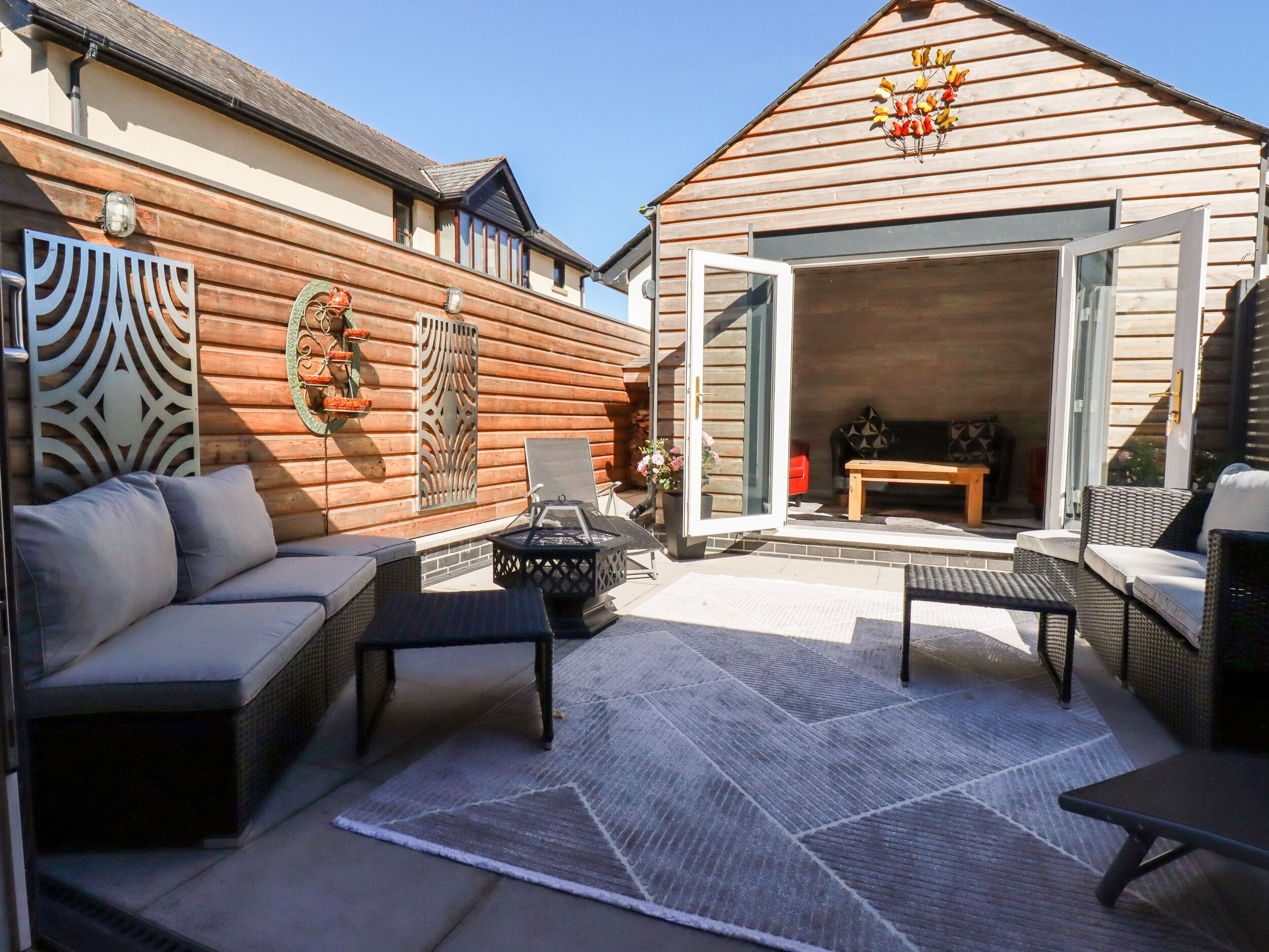 A patio with outdoor furniture, a fire pit, and a wooden building with a glass door.