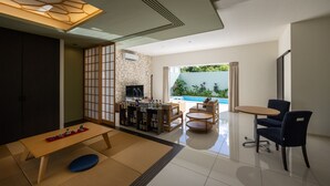A modern living room with a wooden table, sofa, and TV, a stone wall, and a view of a swimming pool. - YUMIHA OKINAWA (Onna)