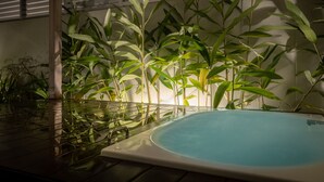 A hot tub surrounded by bamboo plants, with a wooden deck and a white wall in the background. - YUMIHA OKINAWA (Onna)