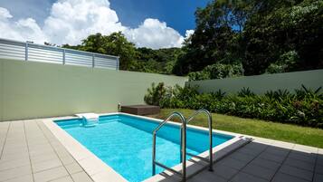Piscina rectangular con una escalera metálica, rodeada por un suelo de baldosas y un muro bajo.