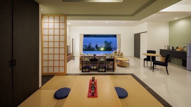 A modern interior with a tatami mat room, a traditional Japanese sliding door, a view of the sea, and a kitchenette area. - YUMIHA OKINAWA (Onna)