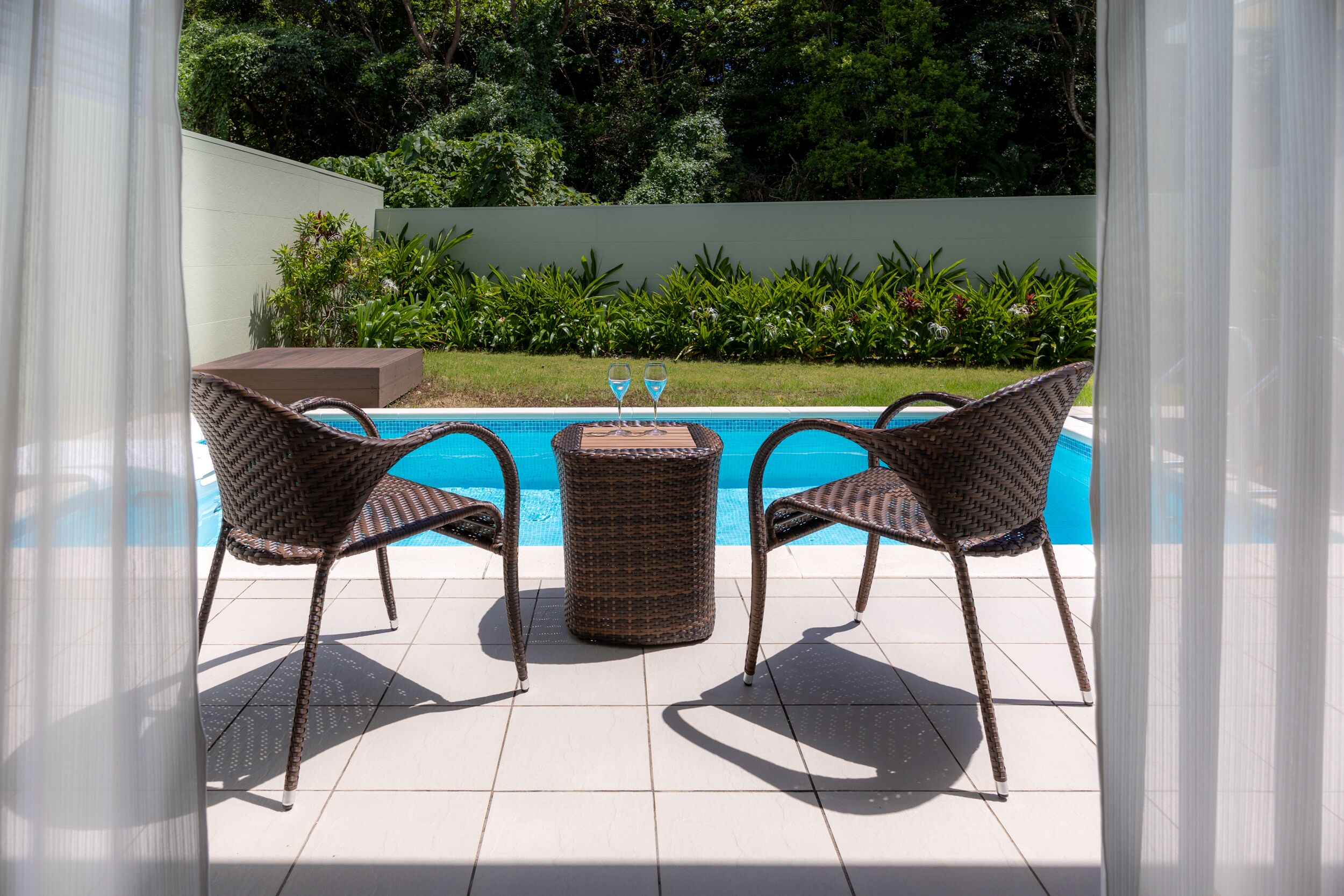 Een terras met twee rieten stoelen en een kleine tafel, met uitzicht op een zwembad.