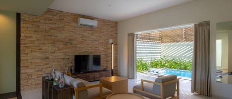 Una sala de estar moderna con una pared de piedra, un televisor de pantalla plana, muebles de madera y vista a una piscina.