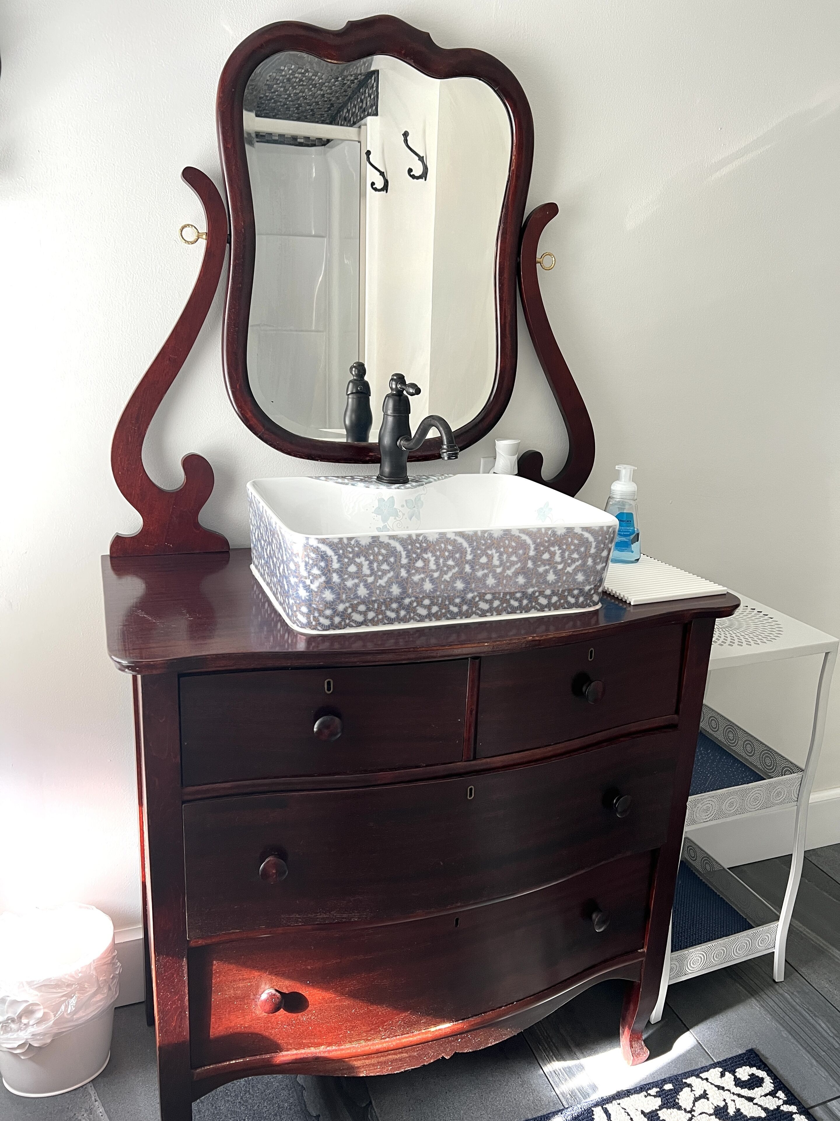 Une commode en bois foncé, surmontée d’un miroir, avec un lavabo blanc en dessous.