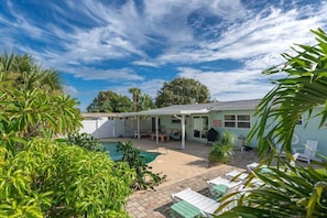 A poolside area with a covered patio, outdoor seating, and lush greenery. - Wow! Beachside Glam 3br wPool, Walk to Park, Beach (Satellite Beach)