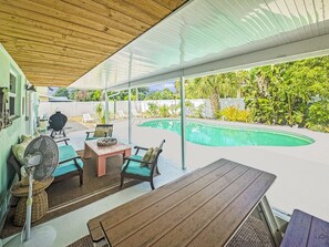 An outdoor patio with a wooden table, two chairs, a fan, and a pool in the background. - Wow! Beachside Glam 3br wPool, Walk to Park, Beach (Satellite Beach)