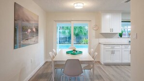 A dining area with a table, chairs, a painting, and a view of a backyard with a pool. - Wow! Beachside Glam 3br wPool, Walk to Park, Beach (Satellite Beach)
