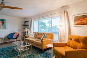 A living room with a sofa, armchair, glass coffee table, and a bookshelf. - Wow! Beachside Glam 3br wPool, Walk to Park, Beach (Satellite Beach)