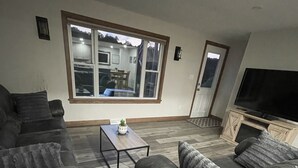 Ein Wohnzimmer mit großem Fenster, einer Sofagarnitur, einem Couchtisch und einem Fernseher.