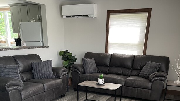 Ein modernes Wohnzimmer mit grauem Ecksofa, einem Couchtisch und einem großen Fenster mit Jalousien.