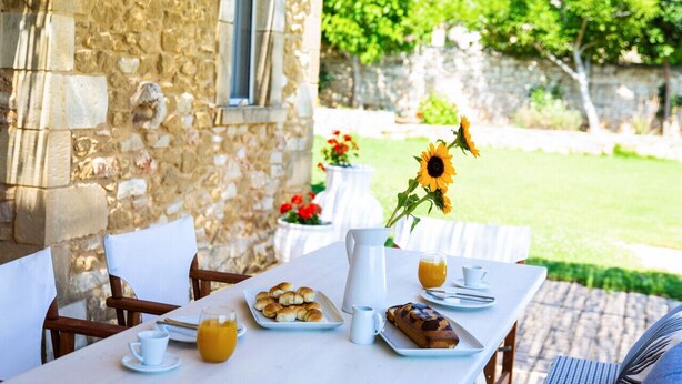 Ein Steinhaus mit einem Frühstückstisch, der Croissants, Brot und einen Saftkrug mit Orangensaft zeigt.
