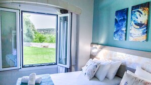 Ein Hotelzimmer mit Bett, einem Fenster mit Vorhängen und zwei abstrakten Bildern an der Wand.