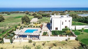 Una villa moderna con piscina, rodeada de exuberante vegetación y vista al mar.