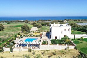 A modern villa with a pool, surrounded by lush greenery and a view of the sea.