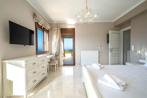 A bedroom with a bed, a dresser, a TV, and a view of the sea.