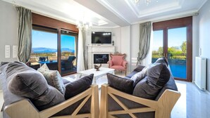 Un salón amplio con chimenea, televisor y vistas a una piscina y montañas.