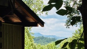 Une cabane en bois dotée d’un balcon donnant sur une forêt dense et des montagnes lointaines.