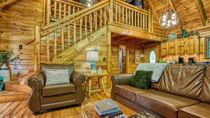 L’intérieur d’une cabane en rondins, avec un escalier en bois, des canapés en cuir, une table basse et un coin cuisine.