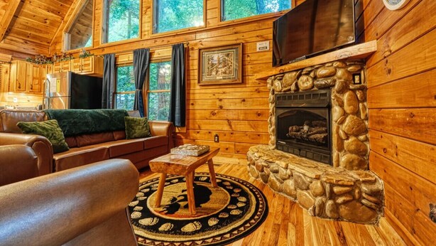 L’intérieur d’une cabane en rondins, avec une cheminée en pierre, des murs en bois, un canapé en cuir et un téléviseur fixé au-dessus de la cheminée.