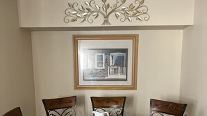 A dining area with a round wooden table, six chairs with cushioned seats, and a framed picture above the table. - Relax On The Coast (Foley)