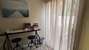 A room with a desk, two chairs, a patterned rug, a painting on the wall, and a window with sheer curtains. - Relax On The Coast (Foley)