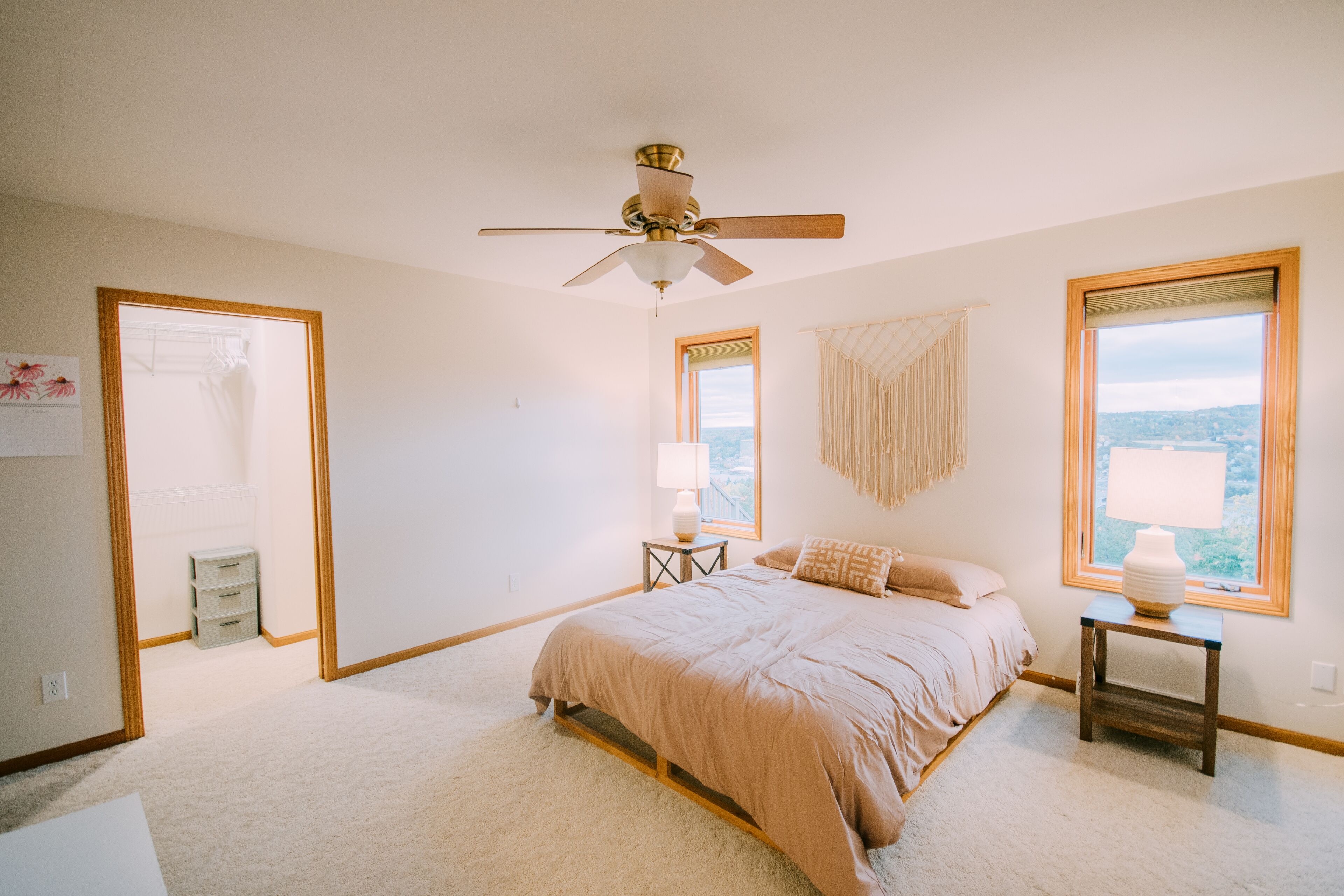 Une chambre à coucher comprenant un lit, un ventilateur de plafond, une table de chevet, une lampe et une fenêtre donnant sur un beau paysage.