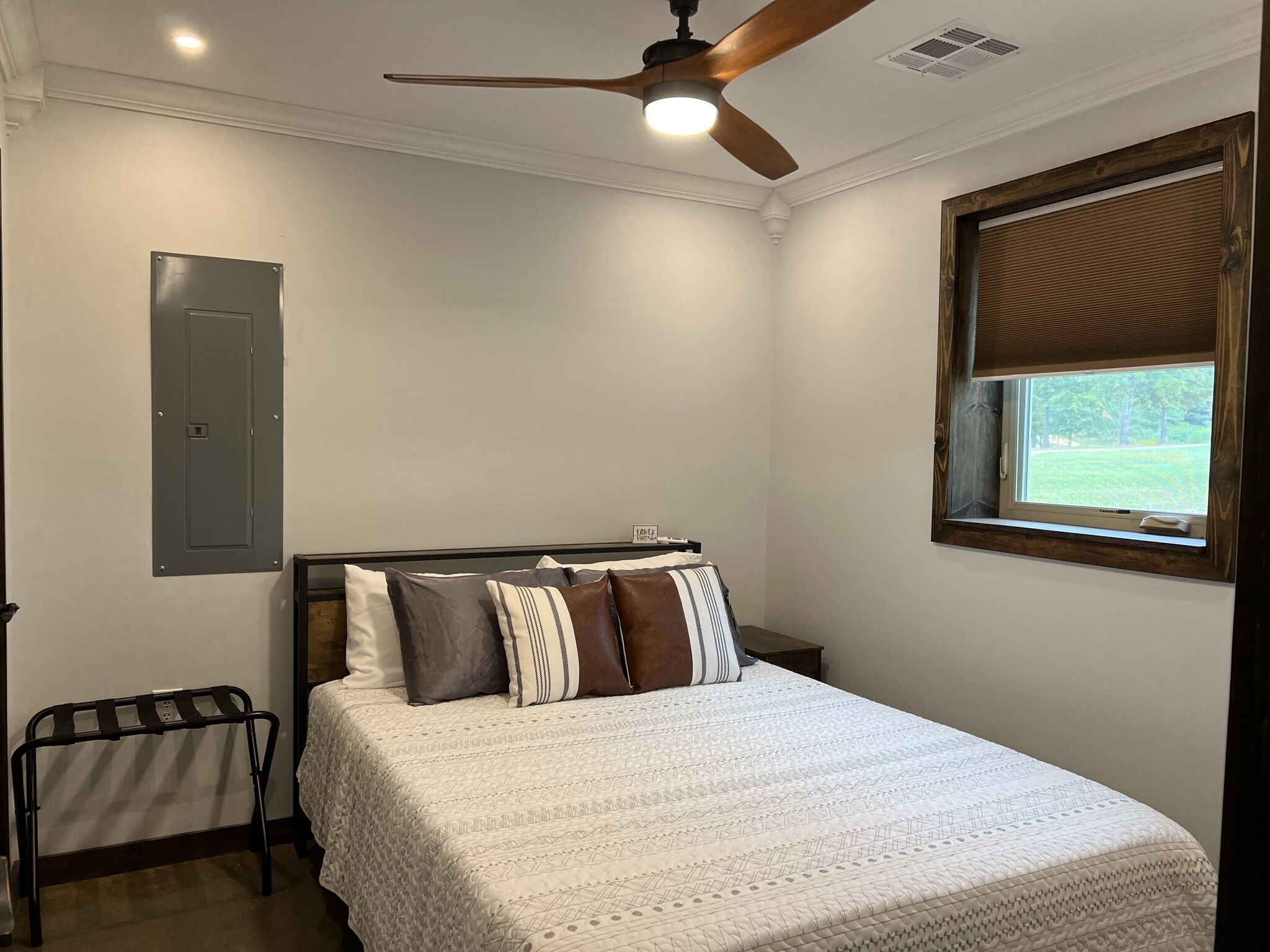 Un dormitorio con cama, ventilador de techo, ventana con persianas, lámpara de pared y radiador.