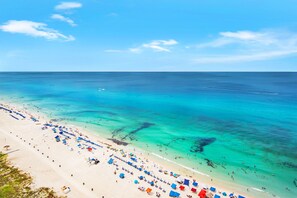 A beach with clear turquoise water, a sandy shore, and numerous umbrellas and beach chairs.