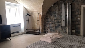 A bedroom with a patterned bedspread, a standing shower, and a stone wall. - TRAMONTANA apartment with whirlpool shower in the room (Taranto)