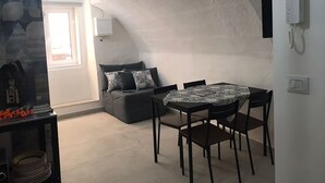 A cozy room with a curved ceiling, a dining table with chairs, a sofa with patterned cushions, and a small kitchen area with a stove. - TRAMONTANA apartment with whirlpool shower in the room (Taranto)