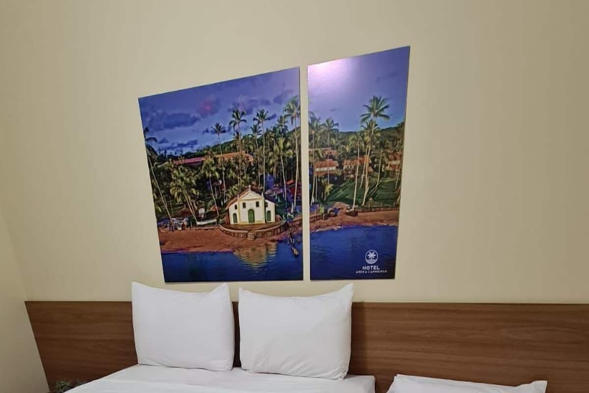 Une chambre d’hôtel avec deux lits simples, une tête de lit en bois et un tableau représentant un paysage côtier.