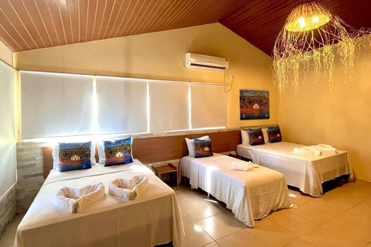 Une chambre d’hôtel avec deux lits simples, une grande fenêtre, un appareil de climatisation et un luminaire suspendu.