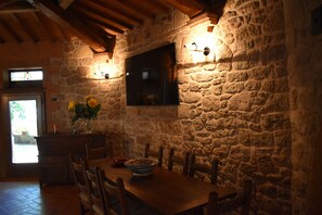 Un coin repas rustique avec des murs en pierre, des poutres en bois au plafond et une grande table entourée de chaises.