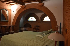 Une chambre avec une arche en briques, un lit avec une literie verte, une lampe de chevet et une chaise.