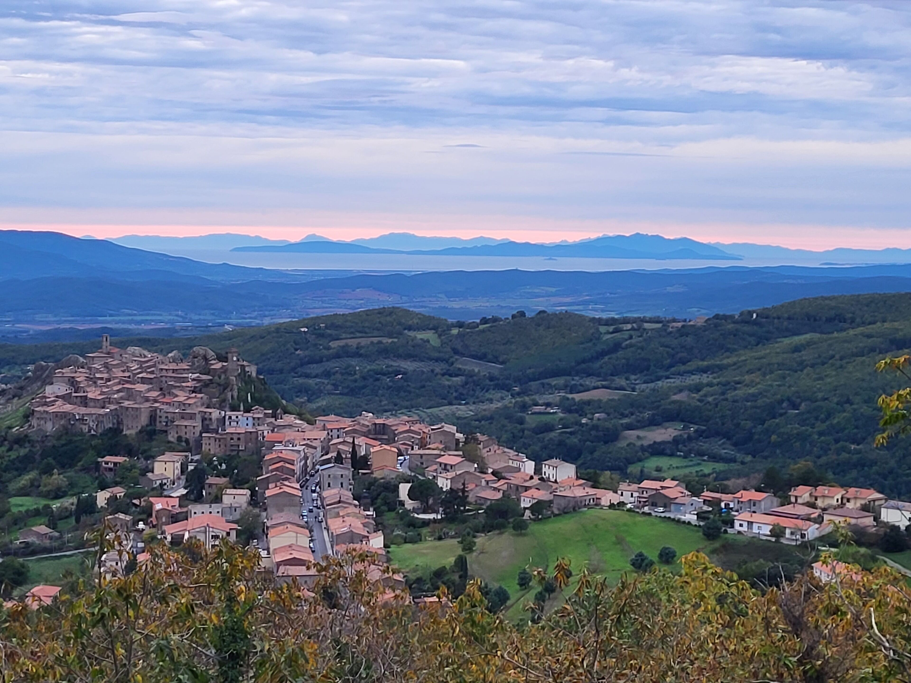 Une ville dotée de bâtiments historiques et d’une église imposante, entourée de collines verdoyantes et bordée par une chaîne de montagnes lointaine.