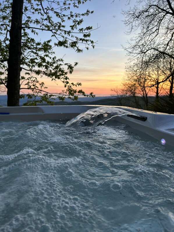 Un bain à remous avec de l’eau en mouvement, entouré d’arbres et avec un coucher de soleil en arrière-plan.