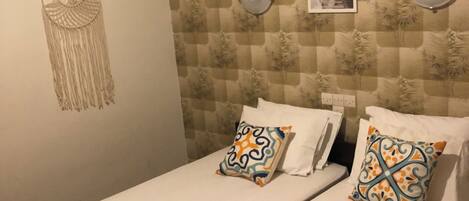 A hotel room with two beds, a yellow bedspread, patterned wallpaper, a wall hanging, and an air conditioning unit.