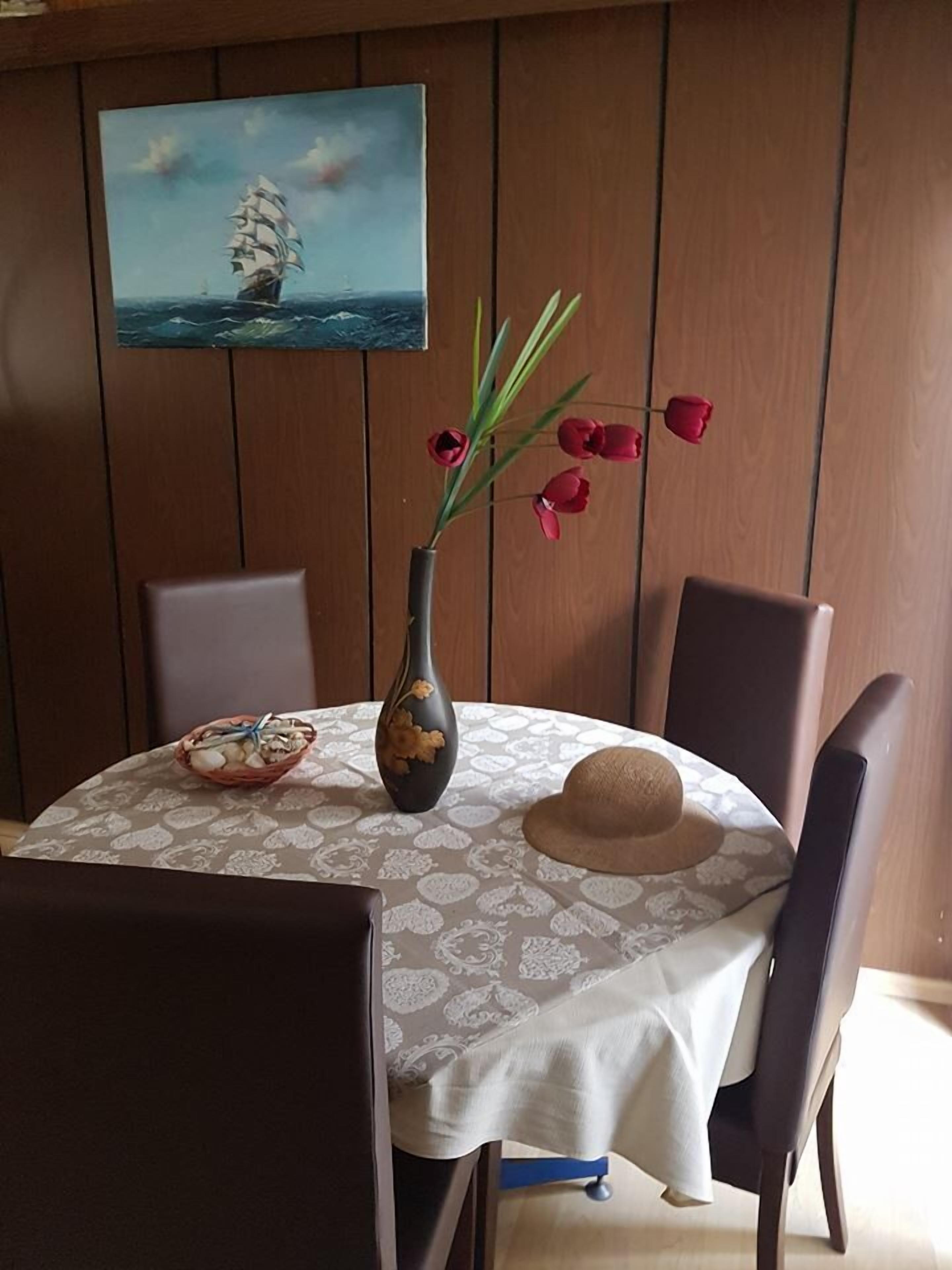 A dining table with a vase of red tulips, a basket of food, and a hat.