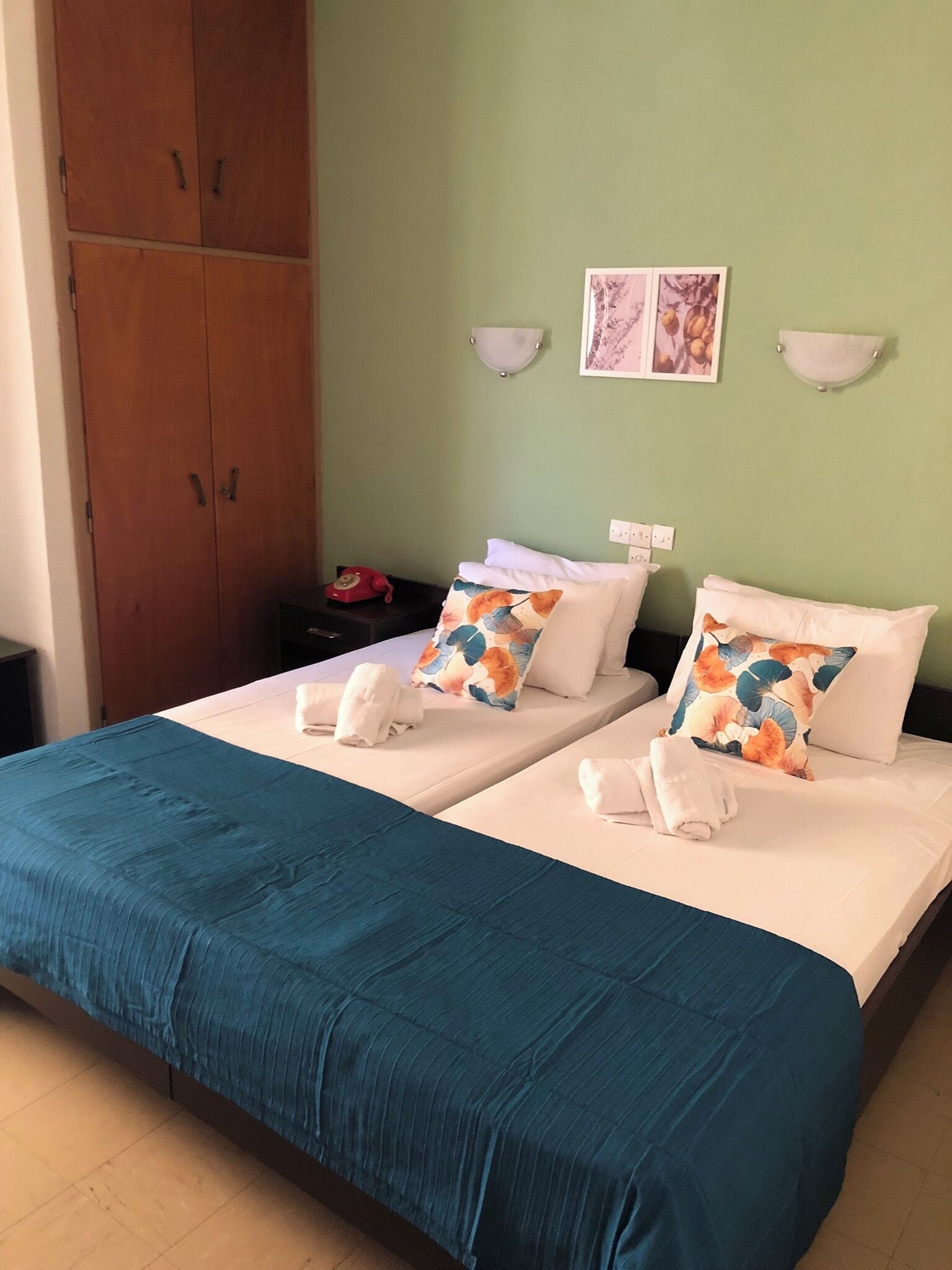Ein Hotelzimmer mit zwei Betten, einem Holzschrank, einem Nachttisch und einer Wandleuchte.