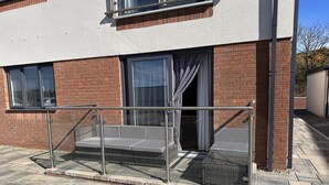 A modern building with a brick facade, a glass balcony with metal railings, and a grey outdoor seating area. - Apartment 3 (Holyhead)