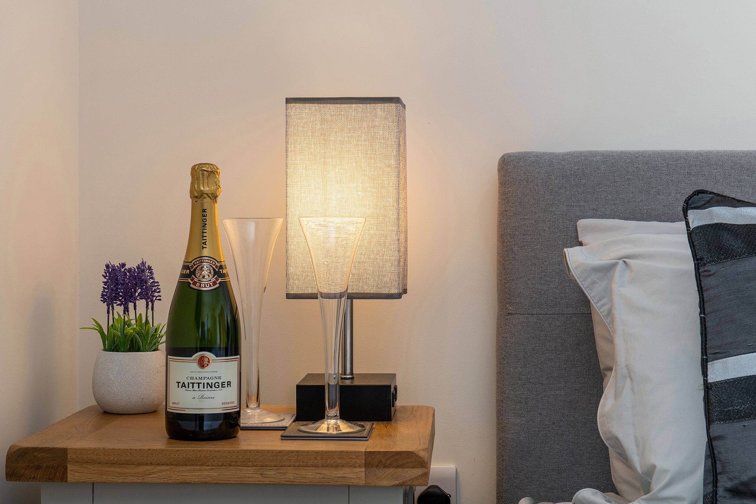 En champagneflaske og en lampe på et natbord ved siden af sengen.